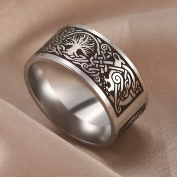 A stainless steel ring with laser etched Tree of Life pattern on it, displayed on a fabric surface.