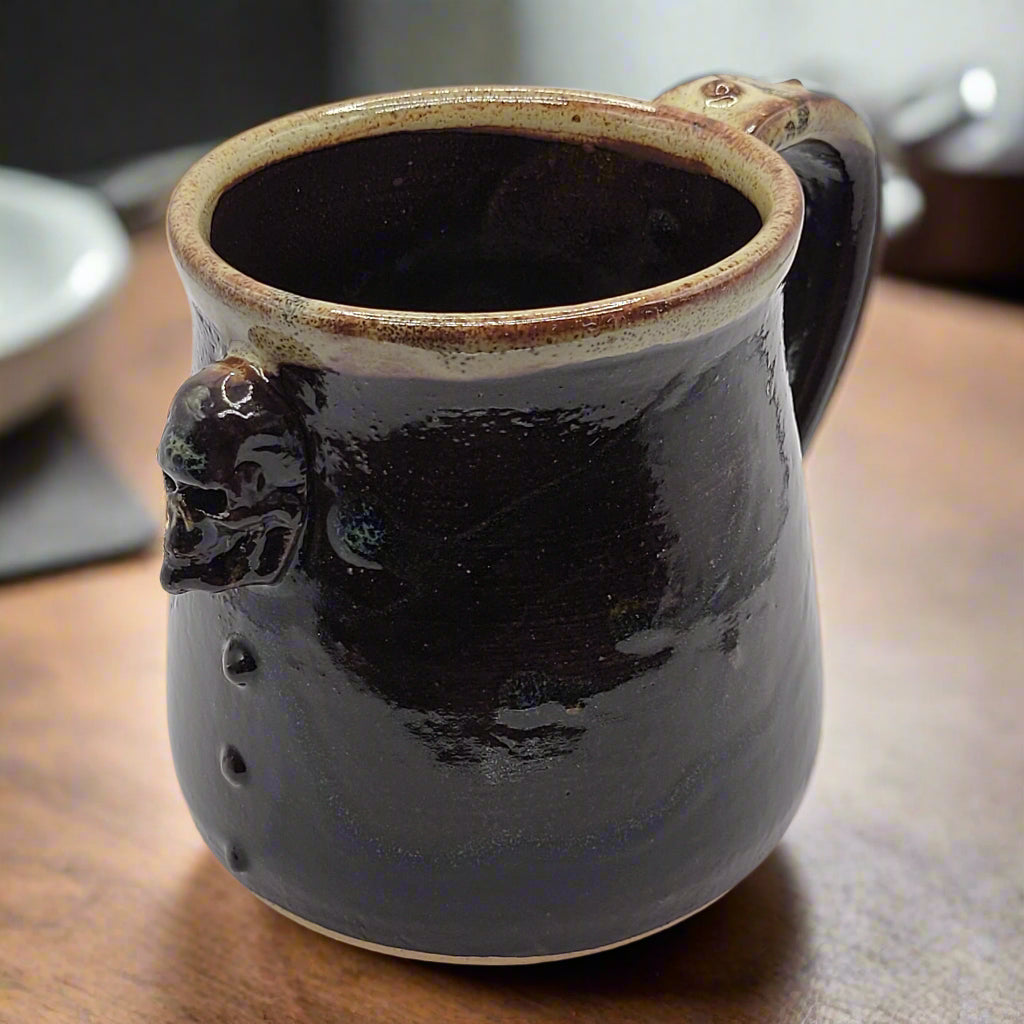 A black ceramic mug with a brown rim and a small decorative skull motif on the side.