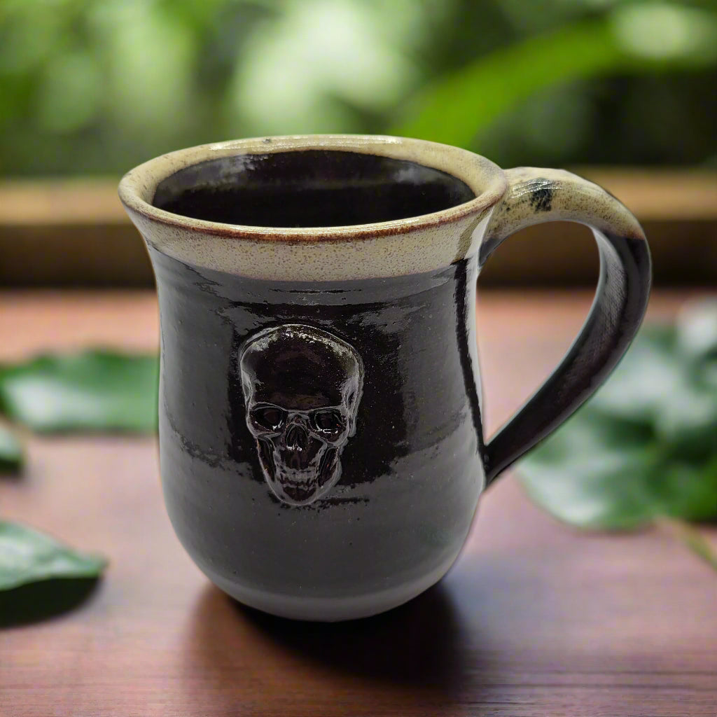 A ceramic mug with a skull design on the front, predominantly dark color with a lighter rim and a skull motif in the center.