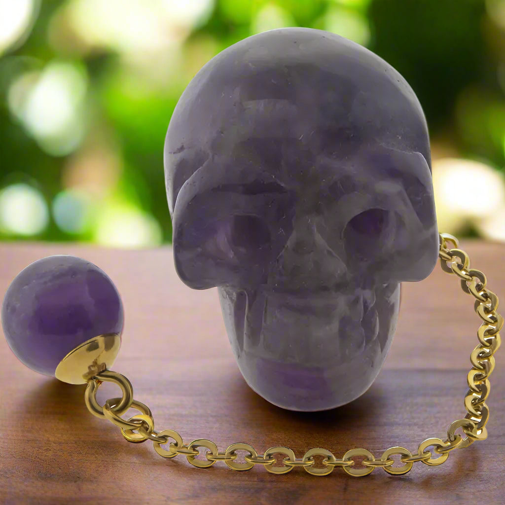 A purple gemstone carved into a skull shape, attached to a gold-colored chain with a small purple sphere at the end.