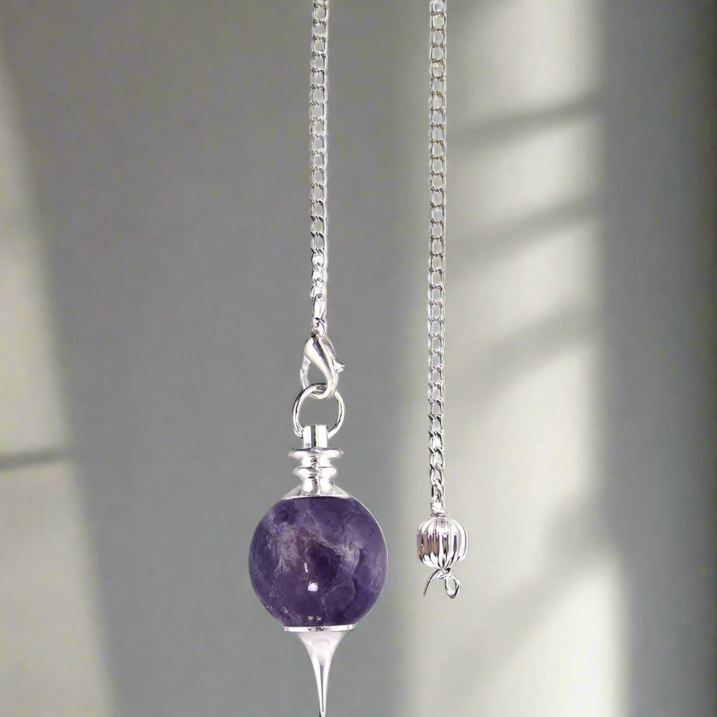 A silver-colored pendulum with a white bead and a small silver ball attached to a chain.