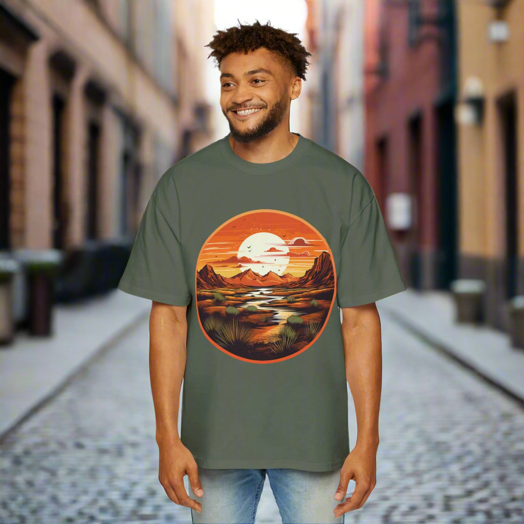 A man wearing a green oversized t-shirt with a graphic print of a sunset and landscape.