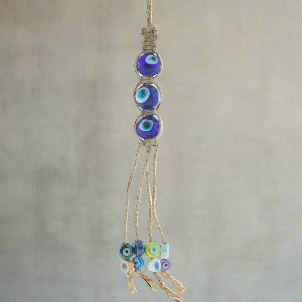 A blue and multicolored glass evil eye talisman on a hemp rope with tassels.