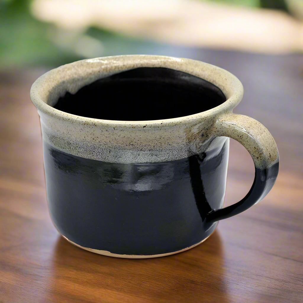 A two-tone ceramic mug with a black bottom and a beige top, featuring a handle on the right side.