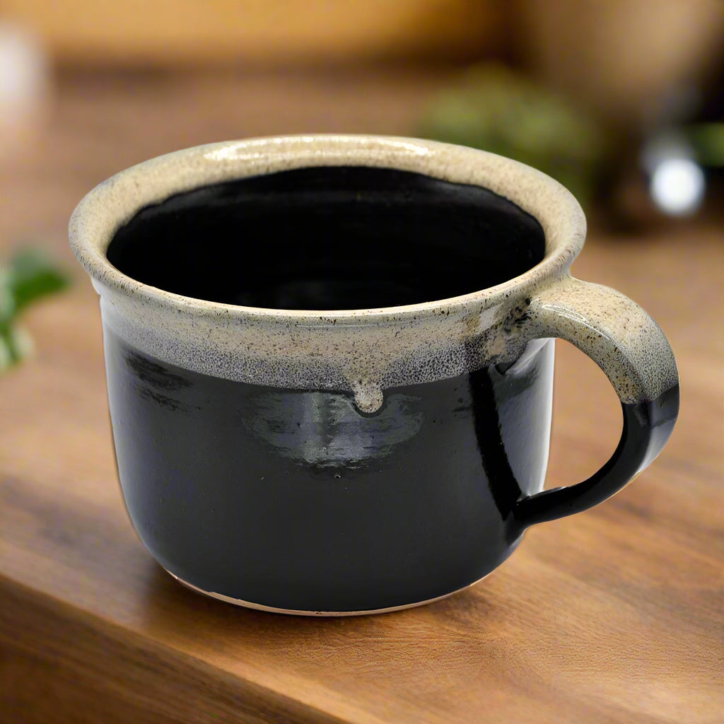 A handmade ceramic mug with a black body and beige rim, photographed on a white background.