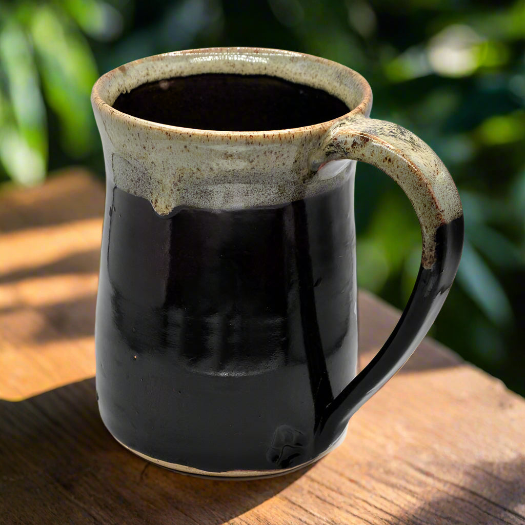 A black ceramic mug with a green and gray rim and handle, handmade in Texas.
