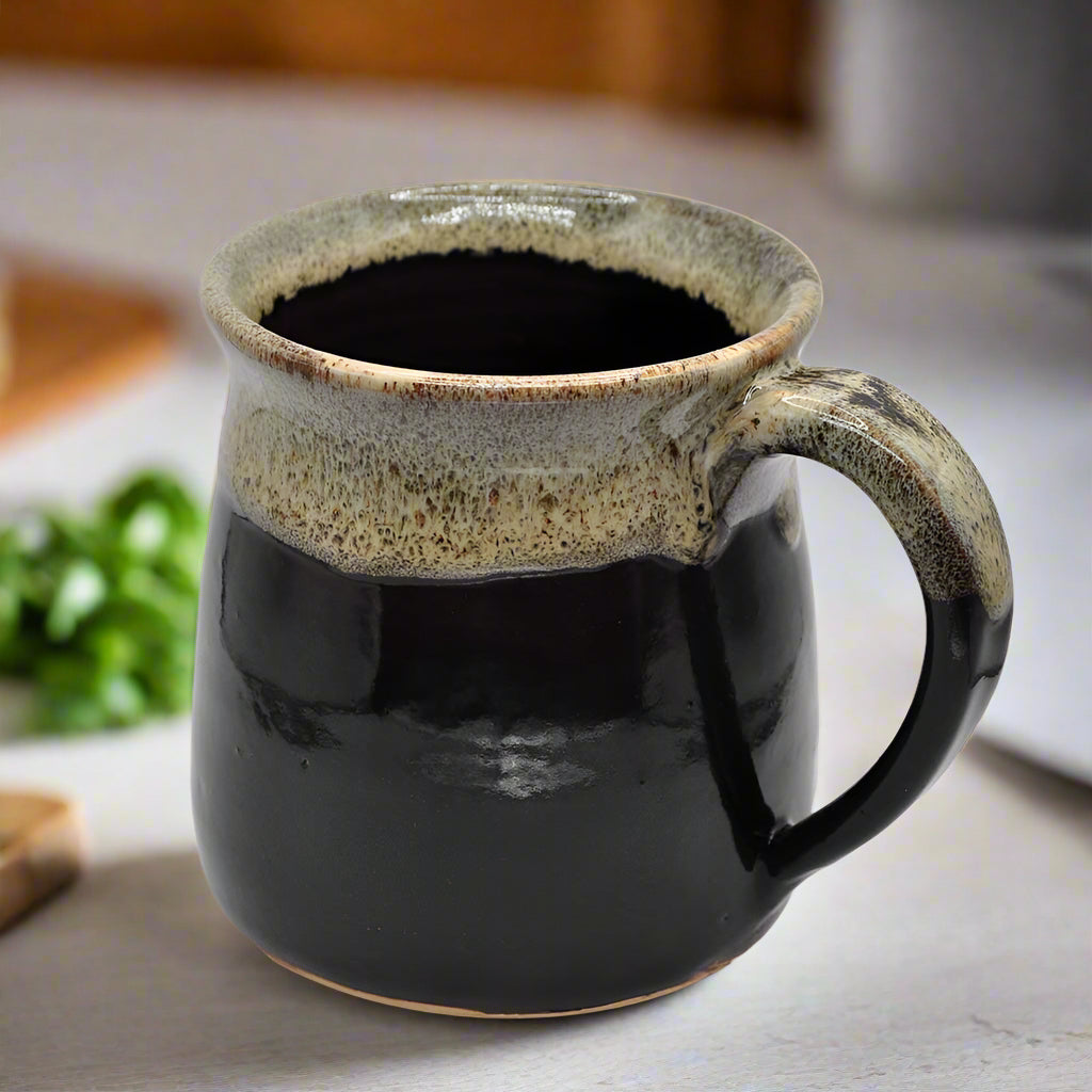 A 16oz black ceramic mug with a beige rim and brown handle, handmade.