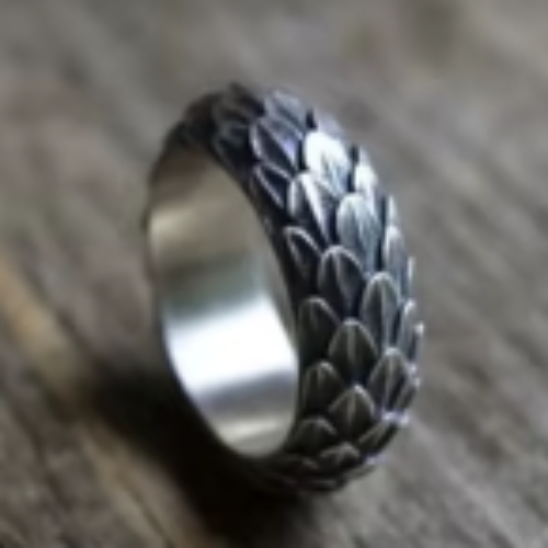 A silver dragon scale ring with a textured design, placed on a wooden surface.