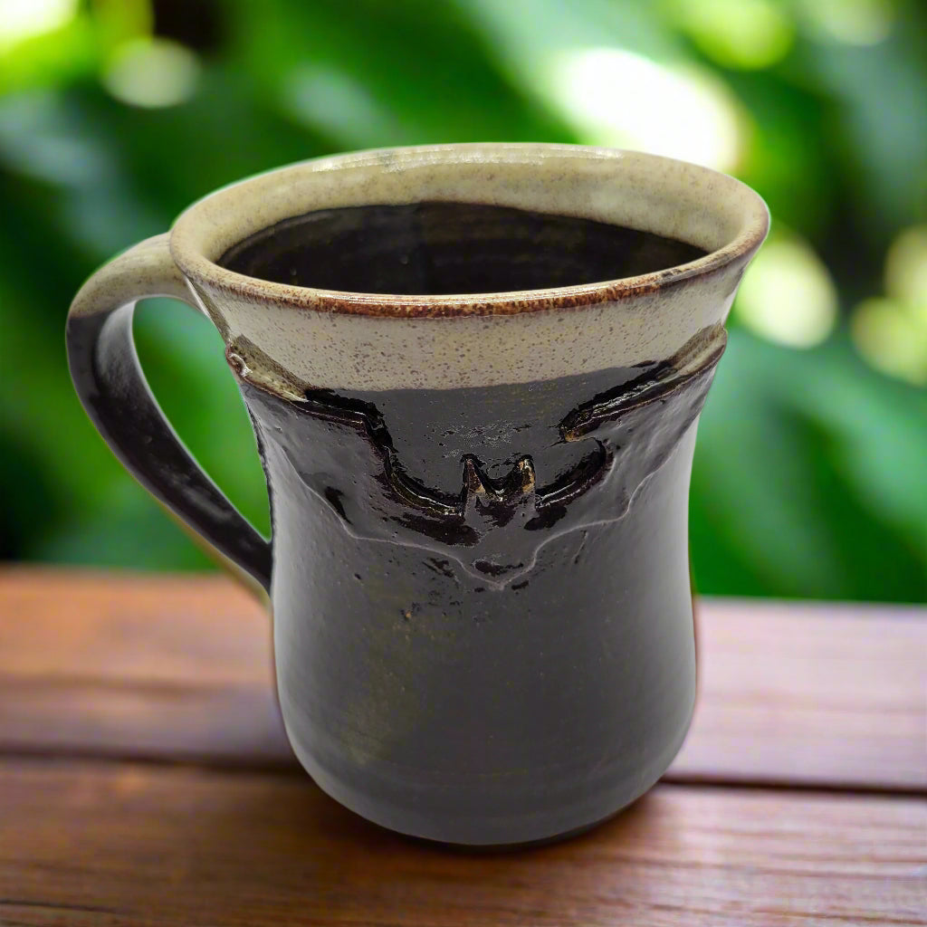 A ceramic mug with a bat design, predominantly dark brown with a lighter brown rim at the top.