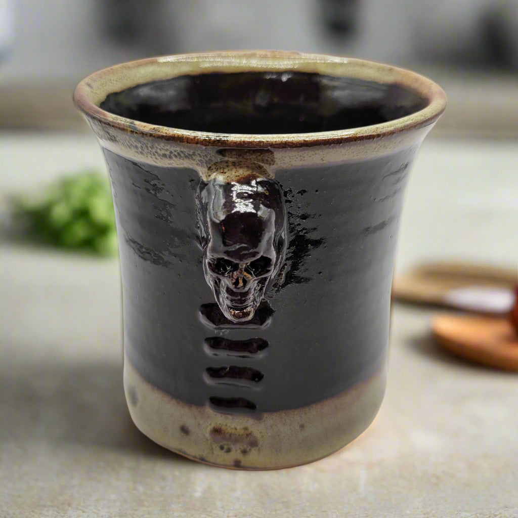 A ceramic mug with a ridged design and a skull motif on the side, predominantly dark in color with a lighter rim.