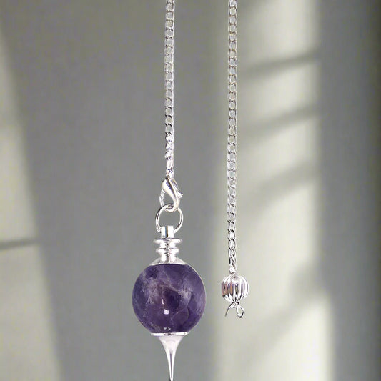 A silver-colored pendulum with a white bead and a small silver ball attached to a chain.